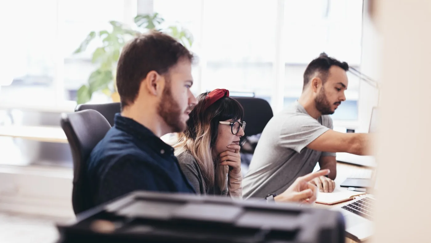 Three colleagues working through a task together at a shared desk